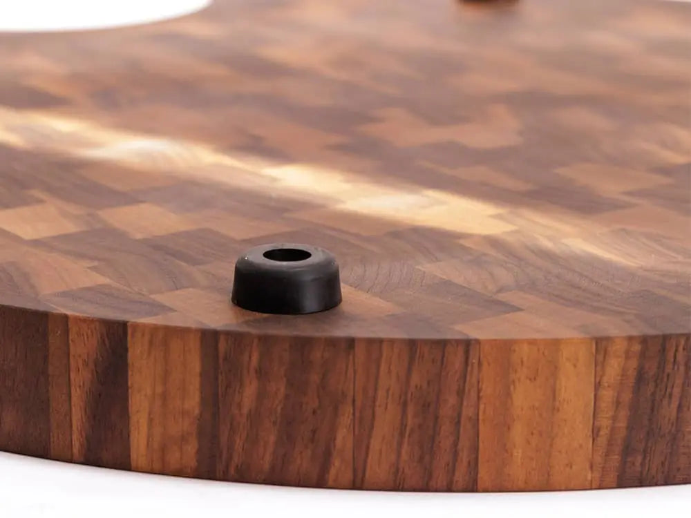 Close-up view of the bottom of a round black walnut end-grain cutting board with a checkered pattern and black rubber feet, against a white background