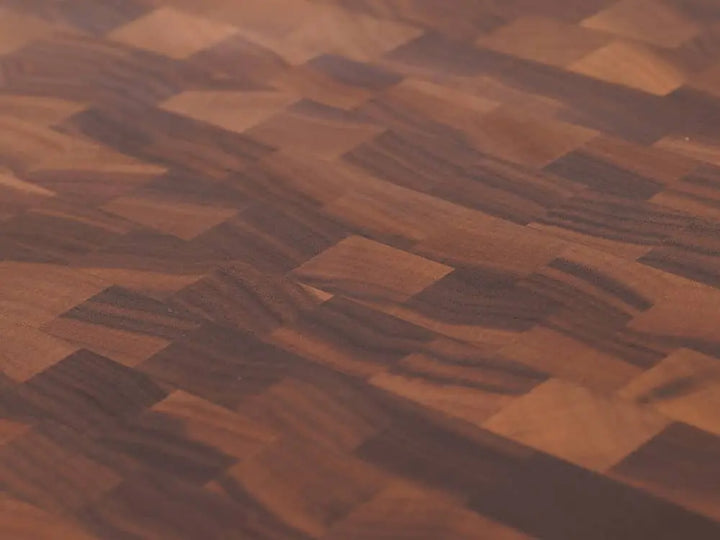 Close-up view of a round, black walnut end-grain cutting board with a checkered pattern of various wood tones, showing the intricate grain and texture