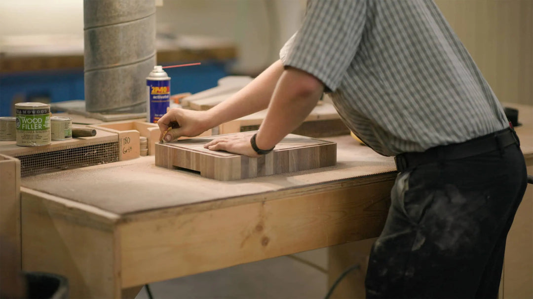 Craftsman sanding a wooden cutting board in a workshop.