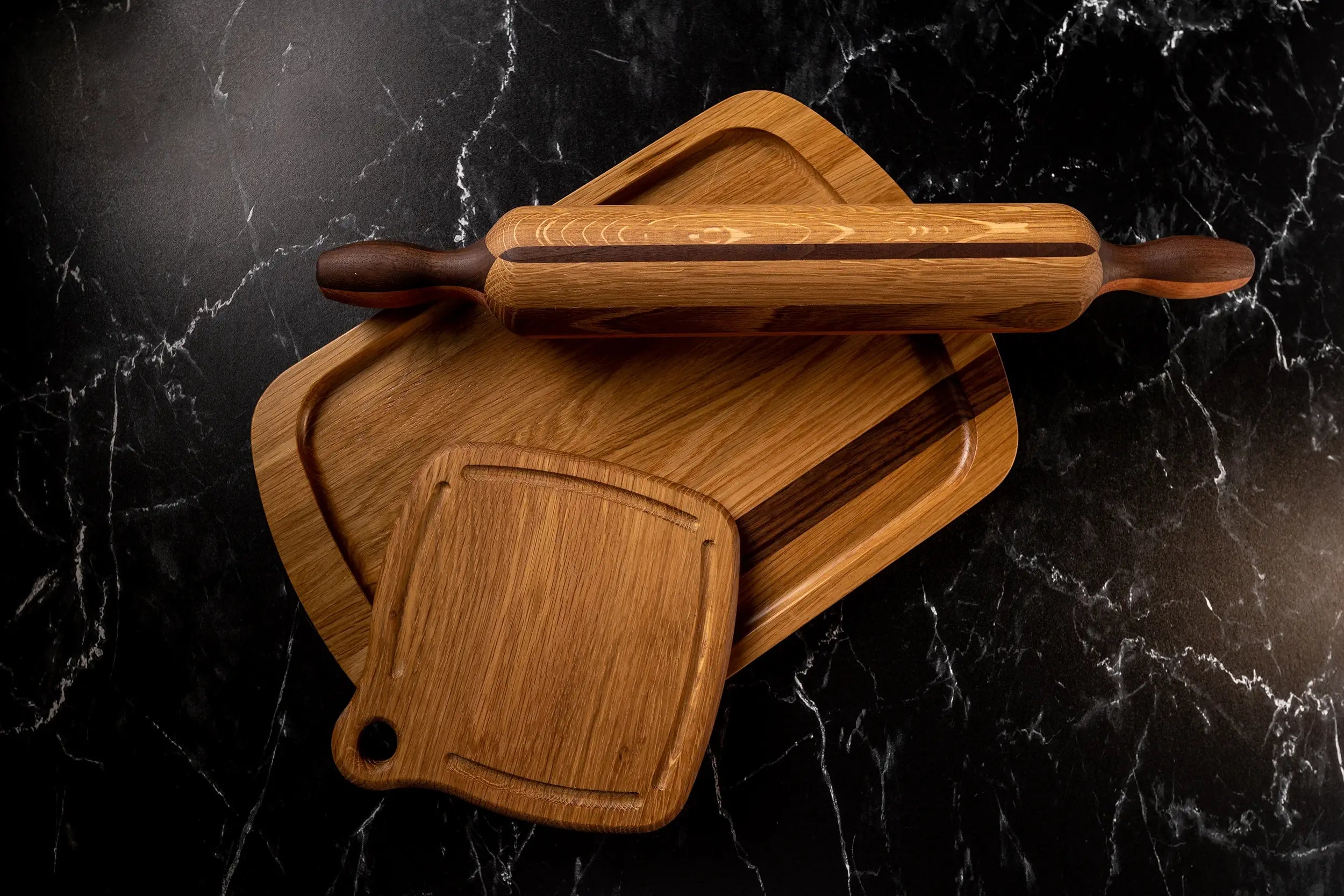 Wooden rolling pin, trivet and serving tray on a dark marble countertop.