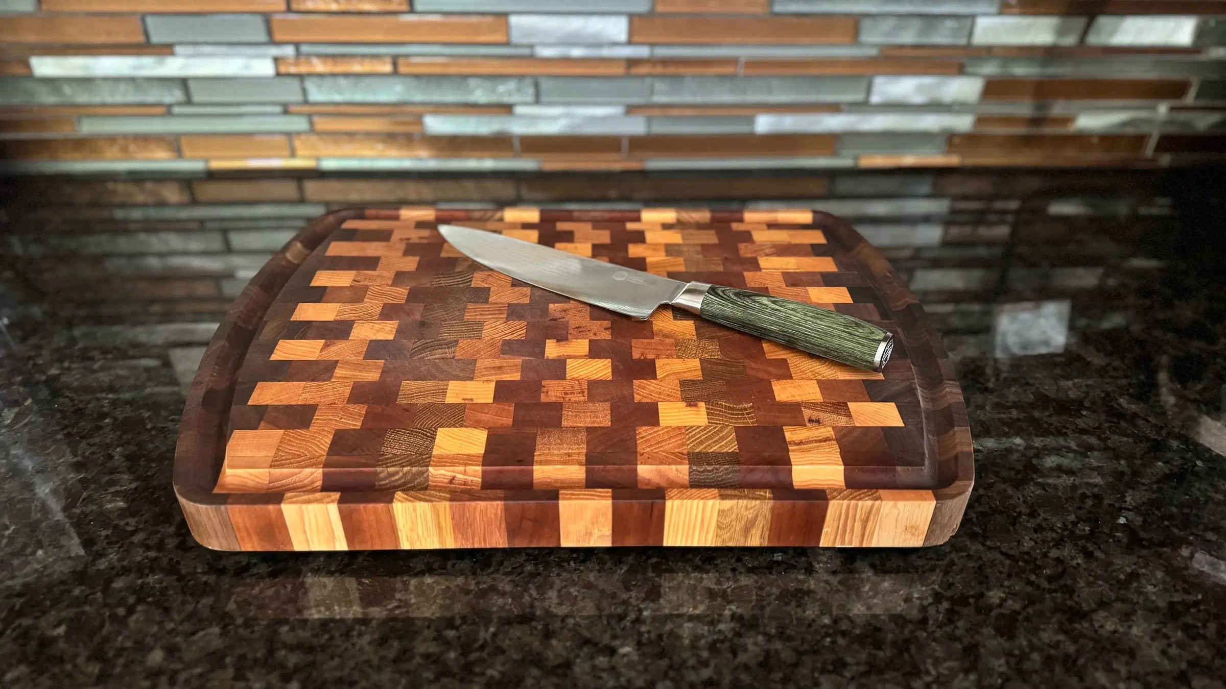 A kitchen knife rests on a checkered wooden cutting board placed on a dark granite countertop.