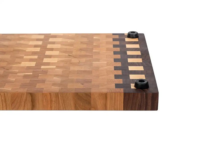 Close-up corner of end grain cutting board showing checkerboard border, thick edge, and non-slip rubber feet