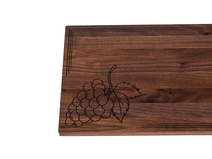 Black walnut charcuterie board with laser-engraved grape cluster design and decorative border detail.