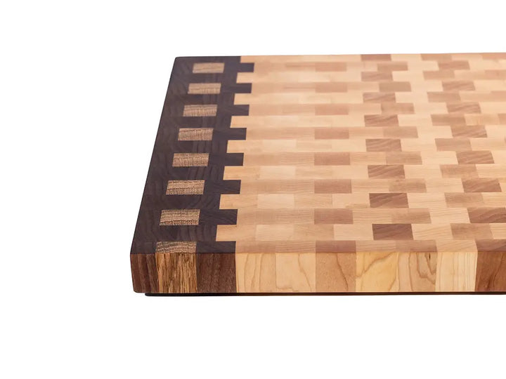 Overhead corner of end grain cutting board showing walnut edge strip with maple inlay pattern and varied tones