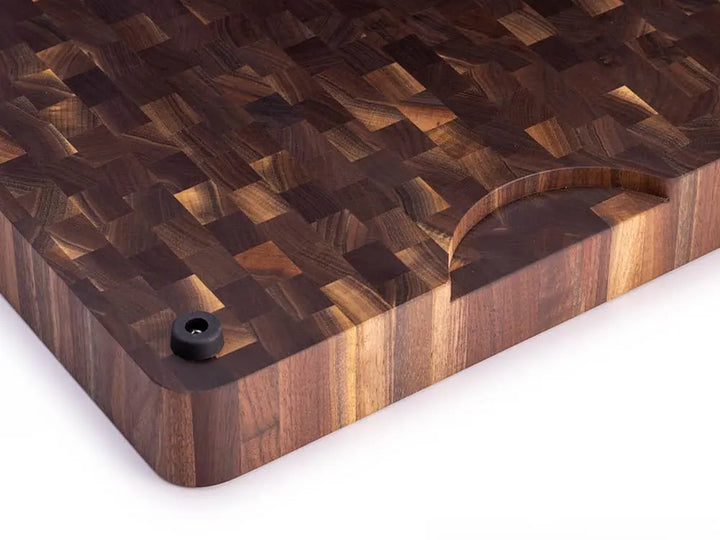 Angled view of a black walnut end grain butcher block with a checkered pattern, handle cutout, and black rubber feet, against a white background