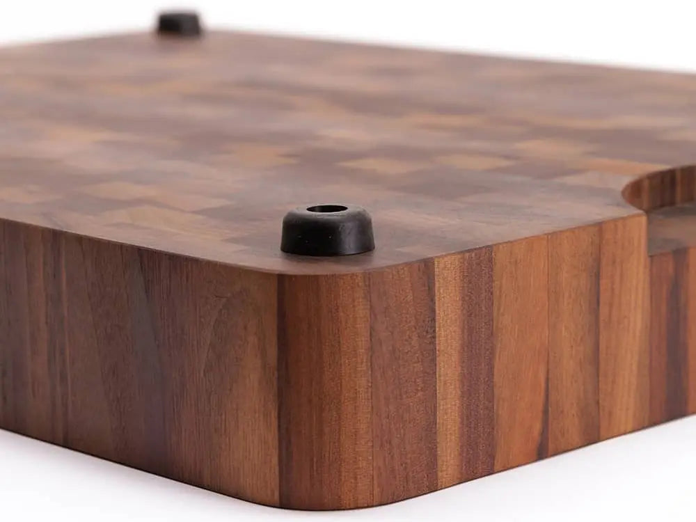 Close-up of a black walnut end grain butcher block with a checkered pattern, handle cutout, and black rubber feet, against a white background