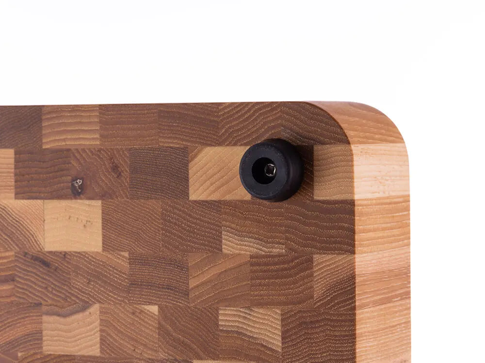 Close-up of the bottom corner of a hickory nut end grain butcher block showing a black rubber foot, against a white background