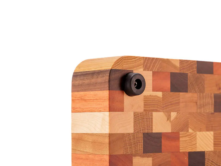 Close-up of the bottom corner of an end grain butcher block with a checkered pattern and a black rubber foot, against a white background