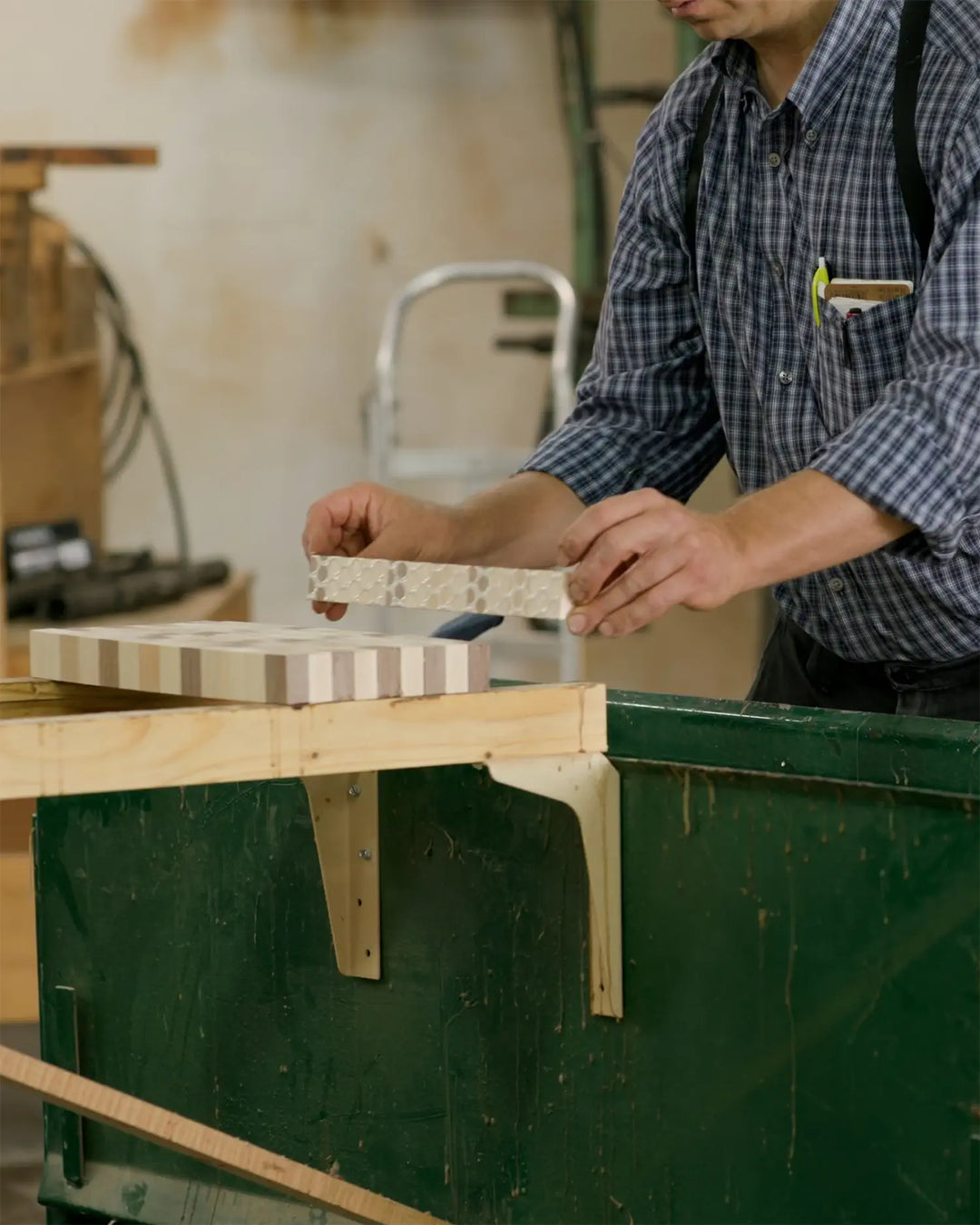 Craftsman assembling an end grain cutting board by aligning and gluing wooden strips on a workbench, highlighting the precision and skill involved in the process