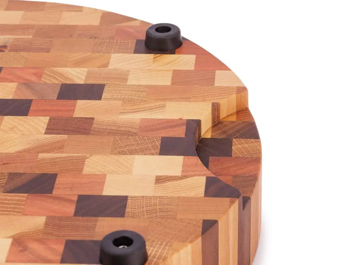 Close-up of a round end grain butcher block with a checkered pattern, featuring non-slip rubber feet and a carved hand grip