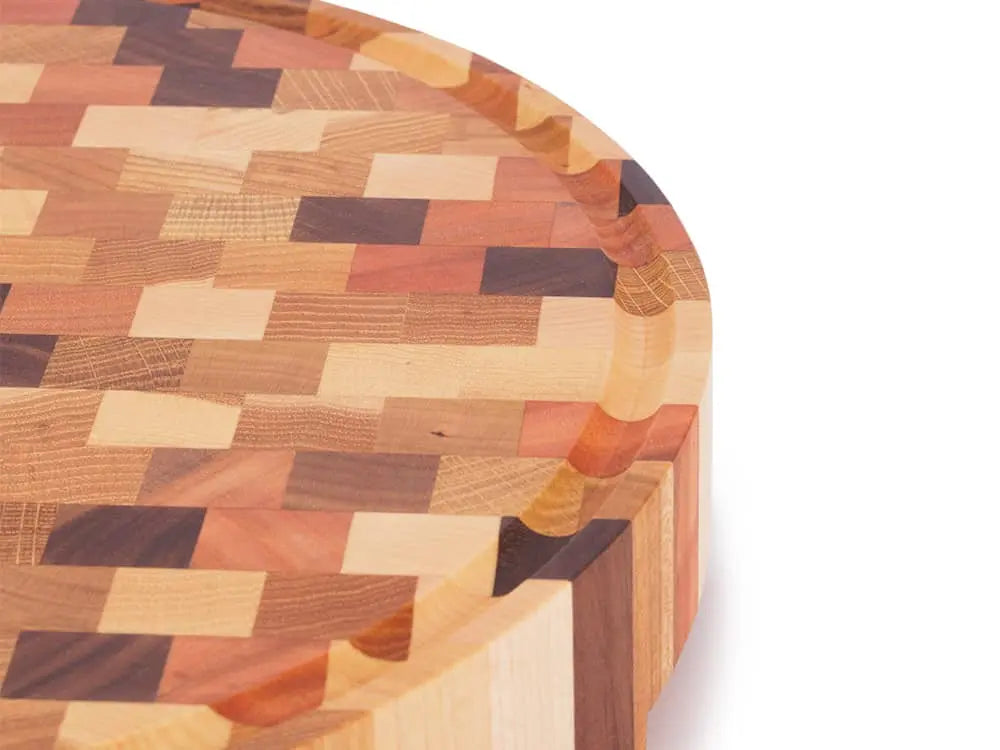 Close-up of a round end grain butcher block with a multicolored checkered pattern and a juice groove around the edge
